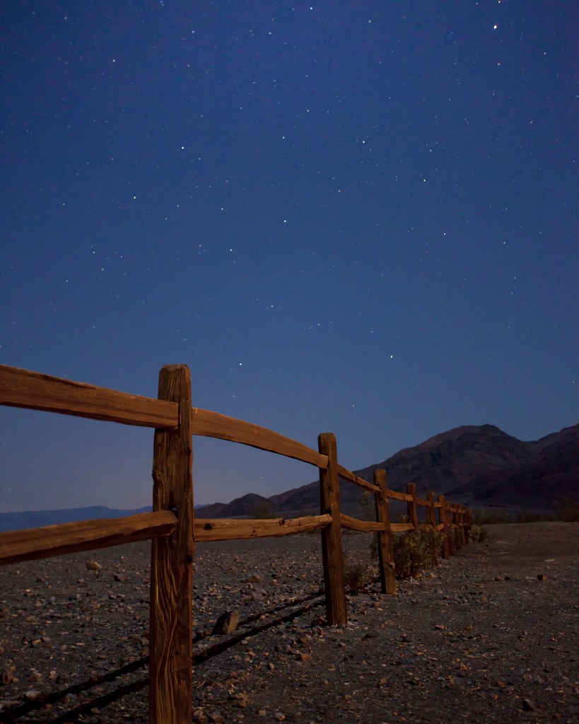 a split-rail fence in moonlight with a star-filled sky